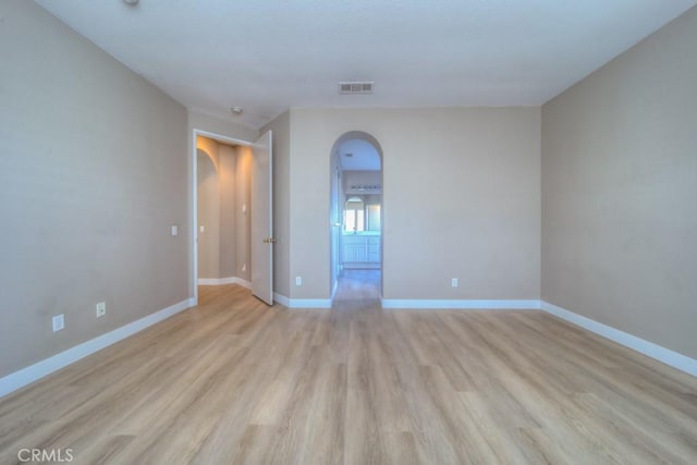 spare room with arched walkways, baseboards, visible vents, and light wood-style floors