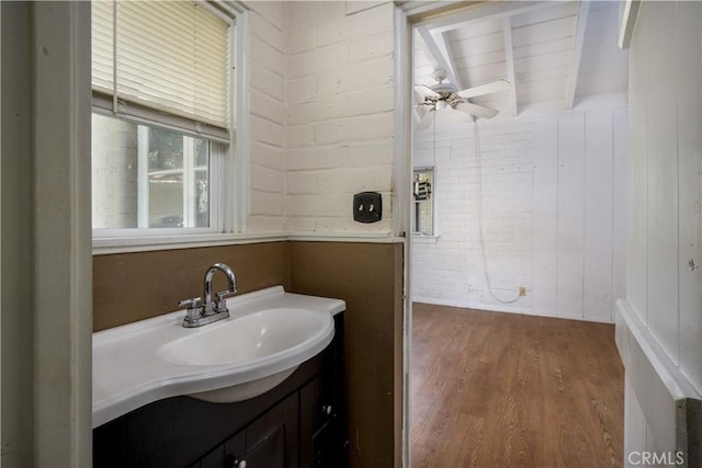 bathroom featuring ceiling fan, wooden walls, wood finished floors, vanity, and beam ceiling