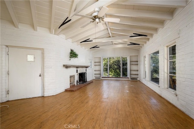 unfurnished living room featuring vaulted ceiling with beams, a fireplace with raised hearth, wood finished floors, and a healthy amount of sunlight