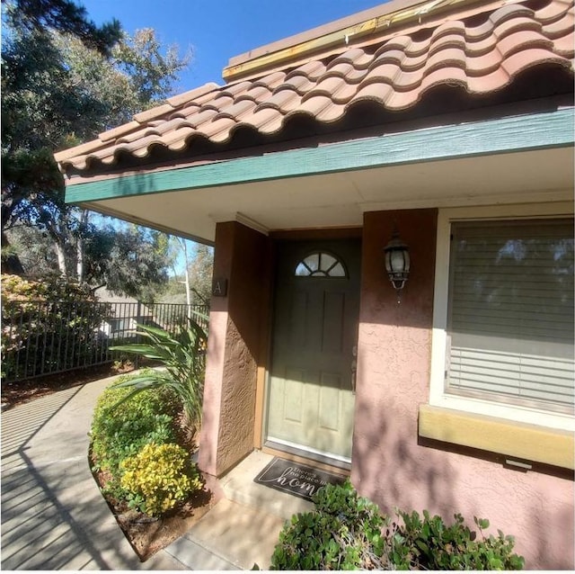 property entrance with a tile roof, fence, and stucco siding