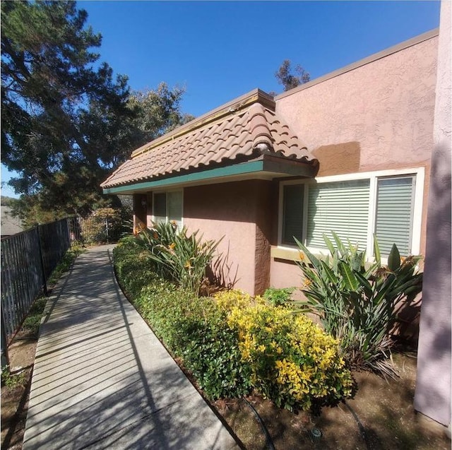 view of side of home featuring a tiled roof, fence, and stucco siding