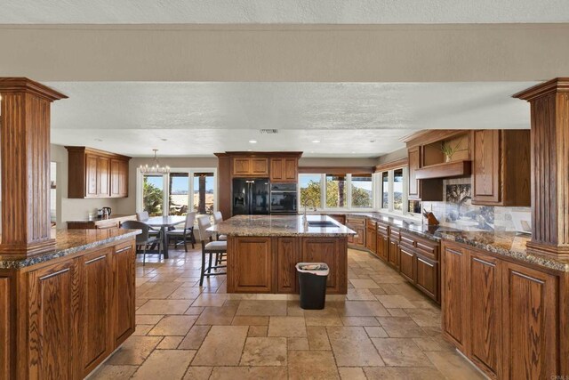 29345 Wilkes Rd, Valley Center, CA 92082 - kitchen featuring black appliances, stone tile floors, a center island, a kitchen bar, and dark stone counters
