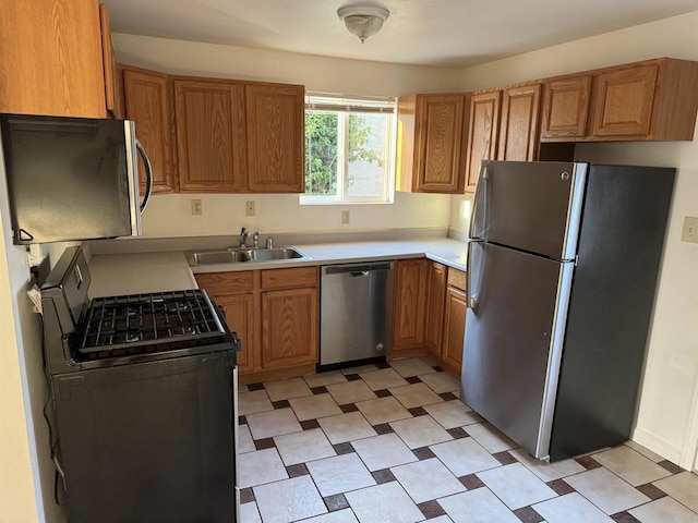 kitchen with brown cabinets, light floors, light countertops, appliances with stainless steel finishes, and a sink