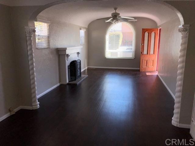 unfurnished living room with arched walkways, a fireplace with raised hearth, dark wood-style flooring, and a healthy amount of sunlight