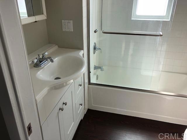 full bathroom featuring wood finished floors, vanity, and bath / shower combo with glass door