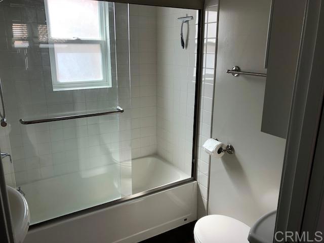 full bathroom with bath / shower combo with glass door and toilet