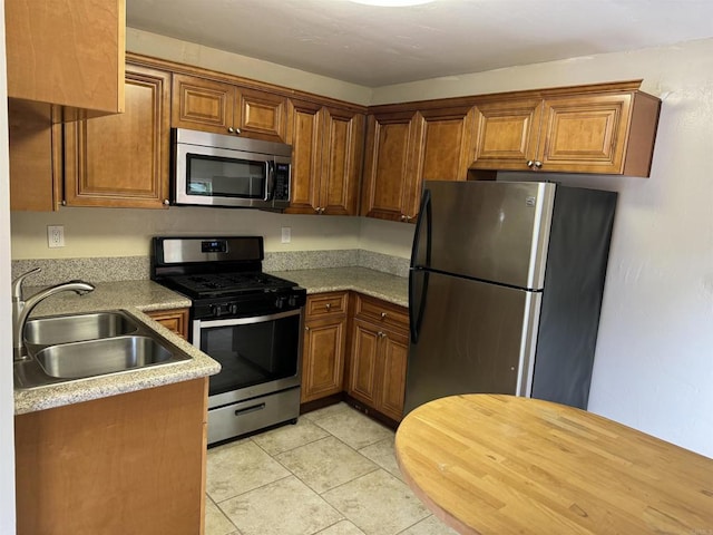 kitchen with light countertops, appliances with stainless steel finishes, brown cabinetry, and a sink