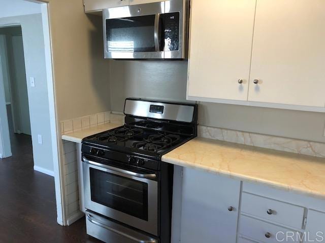 kitchen with stainless steel appliances, white cabinetry, dark wood finished floors, and baseboards