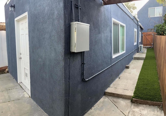 view of side of home with central AC unit, fence, and stucco siding