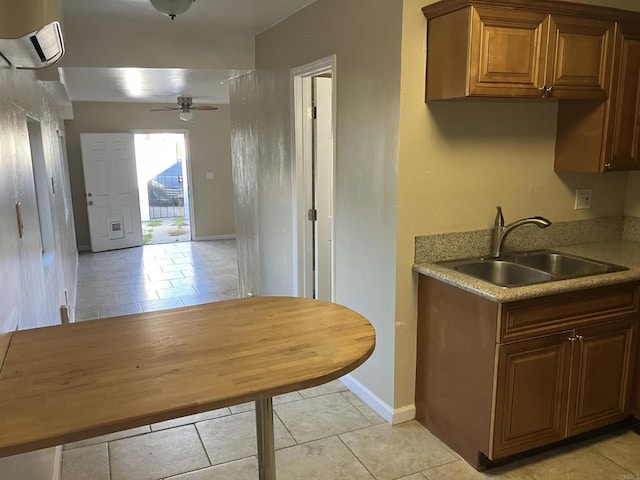 kitchen featuring baseboards, a ceiling fan, light countertops, an AC wall unit, and a sink