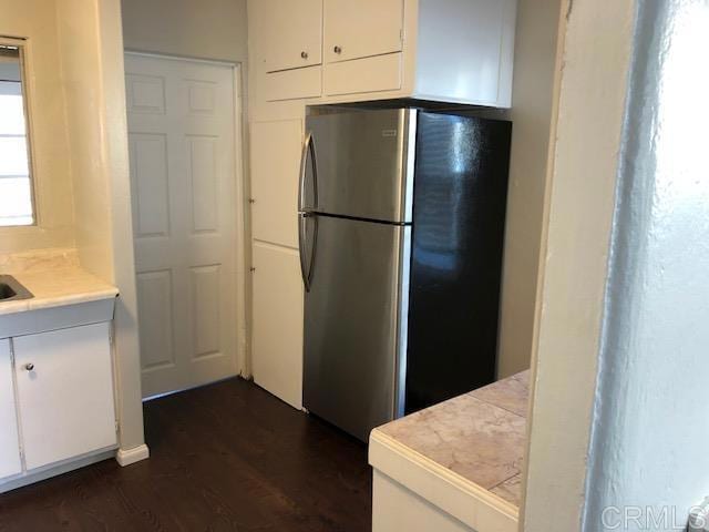 kitchen with dark wood-style floors, freestanding refrigerator, white cabinets, and tile countertops