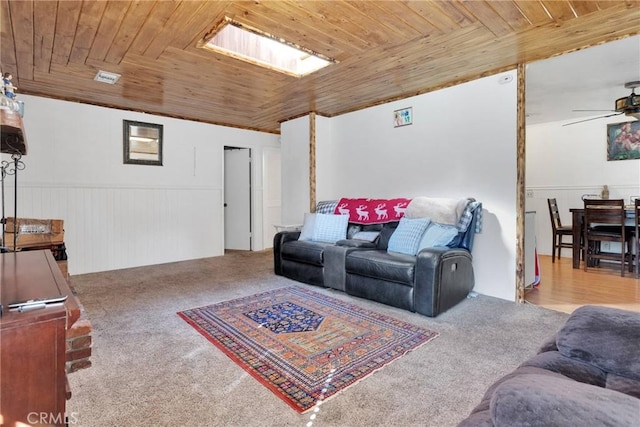 living room featuring wood ceiling, light carpet, ceiling fan, and a wainscoted wall