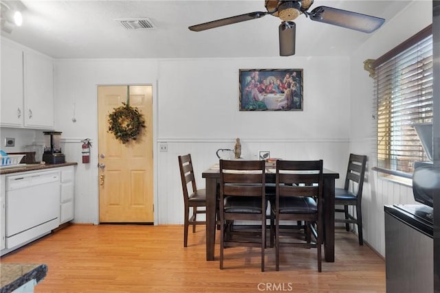 dining room featuring light wood-type flooring, a wainscoted wall, ceiling fan, and visible vents