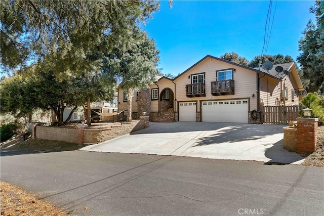 view of front of property with a garage, concrete driveway, a balcony, stone siding, and fence