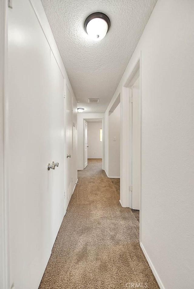 hall with visible vents, a textured ceiling, and light colored carpet