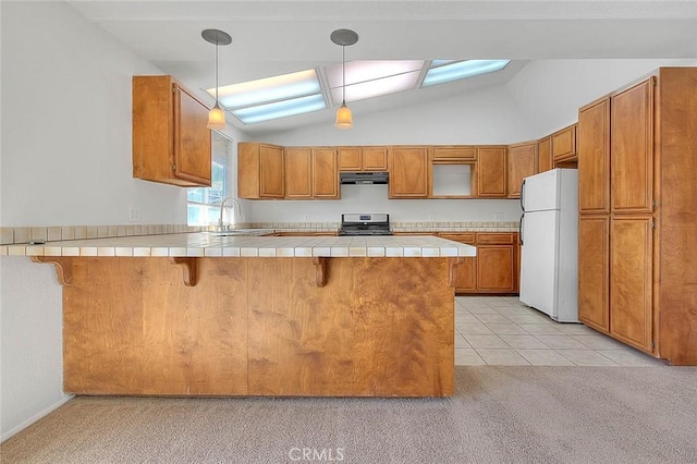 kitchen featuring stainless steel range oven, a peninsula, tile countertops, and freestanding refrigerator