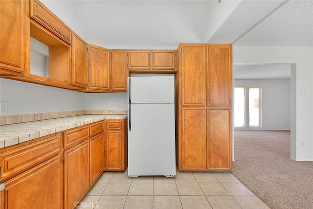 kitchen featuring tile countertops, light tile patterned floors, light carpet, and freestanding refrigerator