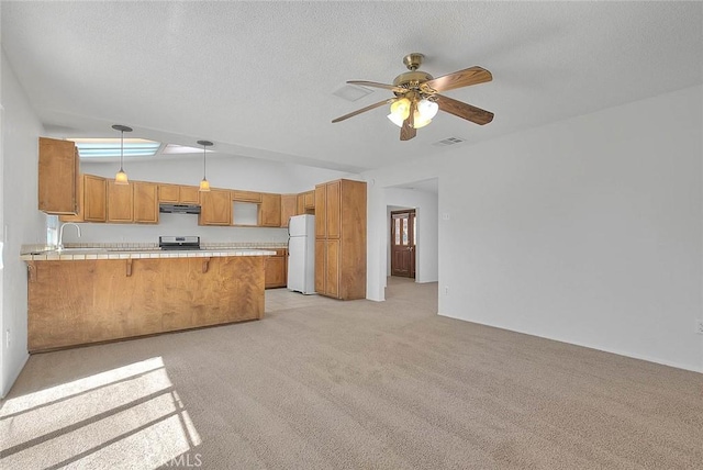 kitchen featuring visible vents, light countertops, freestanding refrigerator, under cabinet range hood, and a peninsula