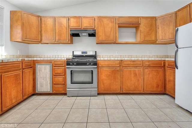 kitchen featuring tile counters, freestanding refrigerator, range hood, vaulted ceiling, and stainless steel range with gas cooktop