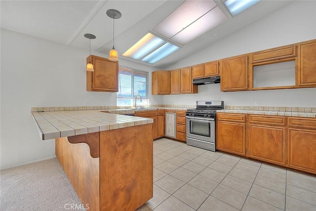 kitchen featuring brown cabinetry, decorative light fixtures, a peninsula, under cabinet range hood, and stainless steel range with gas stovetop