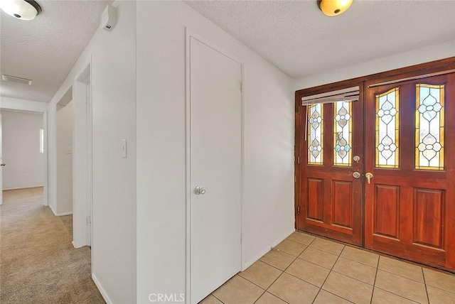 entrance foyer with a textured ceiling, light tile patterned flooring, and light colored carpet