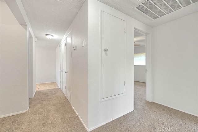 hall featuring a textured ceiling, baseboards, visible vents, and light colored carpet