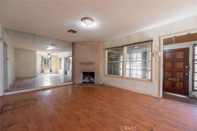 unfurnished living room featuring a fireplace, wood finished floors, visible vents, and baseboards