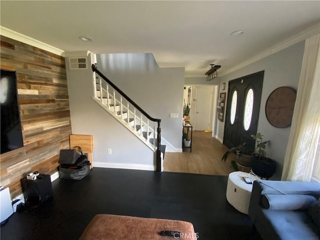 living room with wood walls, wood finished floors, baseboards, stairs, and ornamental molding