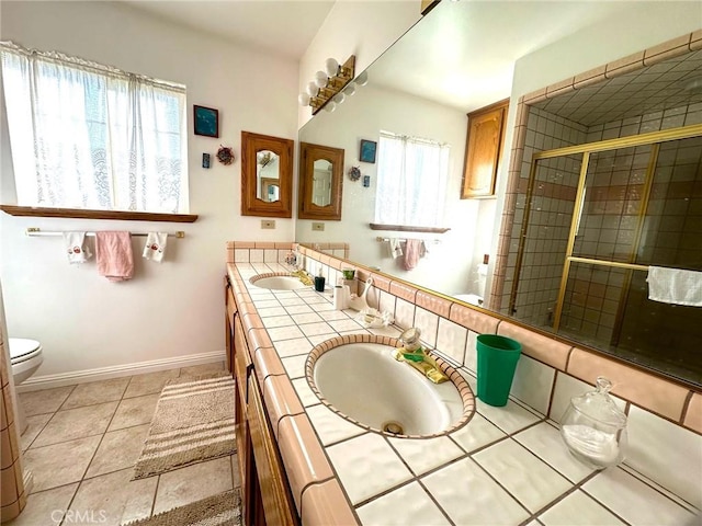 bathroom featuring baseboards, double vanity, tile patterned floors, and a healthy amount of sunlight