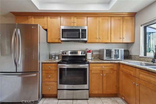 kitchen with brown cabinets, a sink, stainless steel appliances, light tile patterned flooring, and light stone countertops