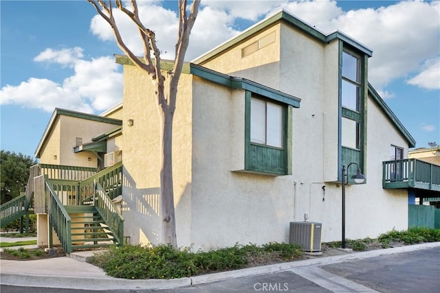 view of property exterior with stairs, central air condition unit, and stucco siding