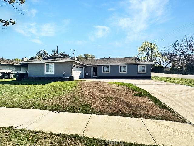 ranch-style house featuring a front yard, concrete driveway, an attached garage, and stucco siding