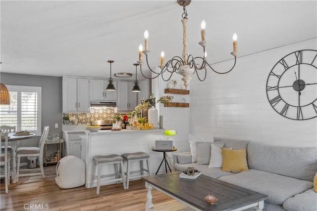 kitchen featuring light wood-style floors, decorative light fixtures, light countertops, under cabinet range hood, and backsplash