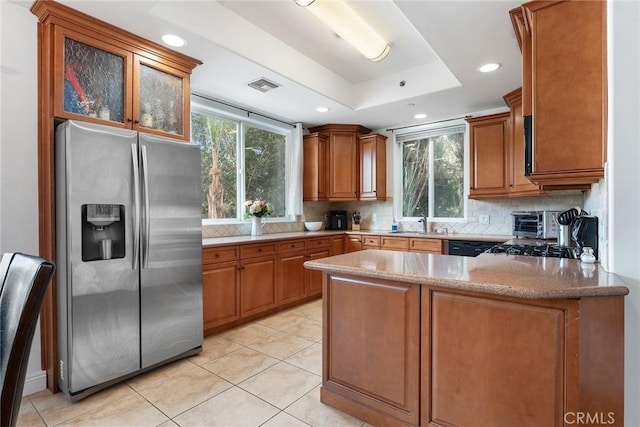 kitchen featuring stainless steel fridge, visible vents, a raised ceiling, glass insert cabinets, and a peninsula