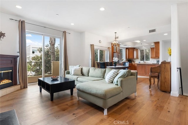 living area with visible vents, a glass covered fireplace, light wood-type flooring, a chandelier, and recessed lighting