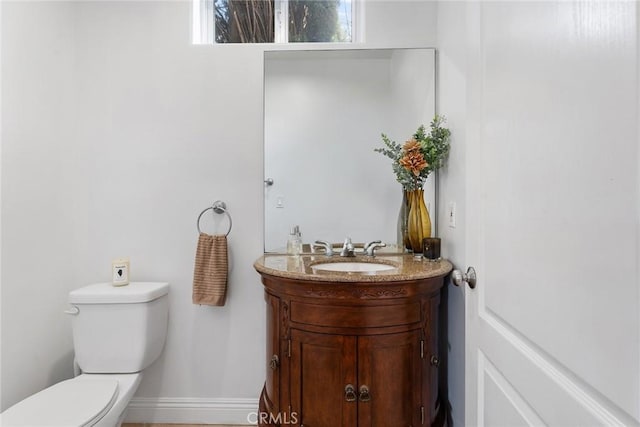 half bath featuring baseboards, vanity, and toilet