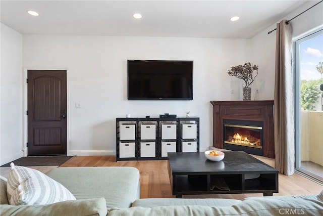 living room with light wood-type flooring, recessed lighting, baseboards, and a glass covered fireplace