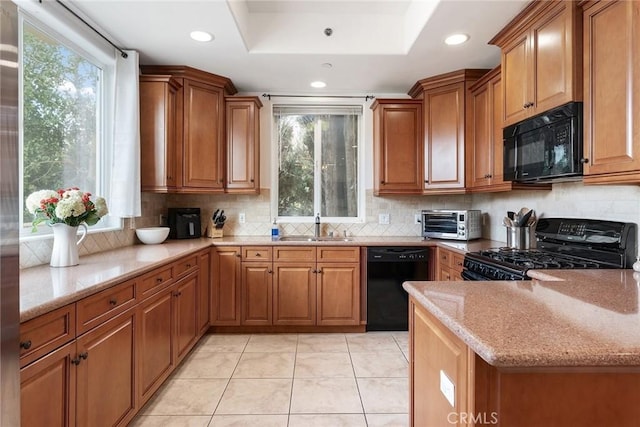 kitchen featuring brown cabinetry, a sink, light stone countertops, black appliances, and backsplash