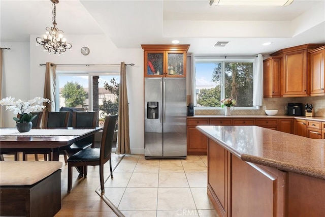 kitchen with glass insert cabinets, pendant lighting, stainless steel fridge, and a raised ceiling