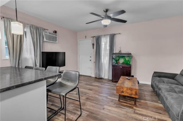 living area with a wall unit AC, ceiling fan, baseboards, and wood finished floors