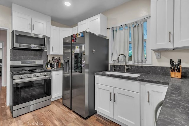 kitchen with light wood-type flooring, appliances with stainless steel finishes, white cabinets, and a sink