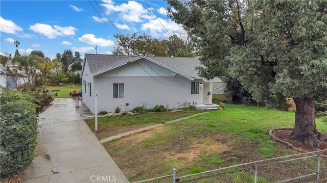 view of home's exterior featuring a yard, fence, a shingled roof, and stucco siding