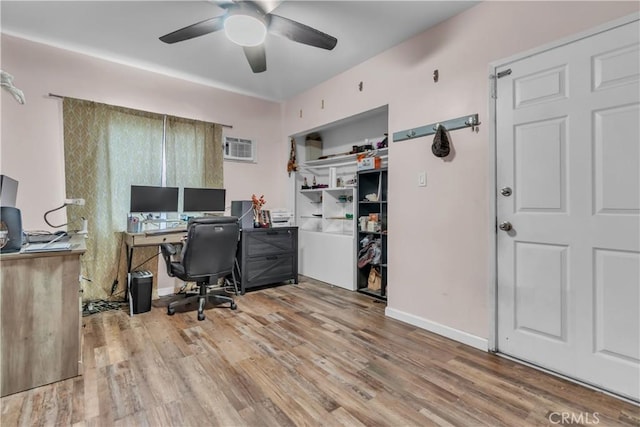 home office featuring a wall unit AC, ceiling fan, baseboards, and wood finished floors