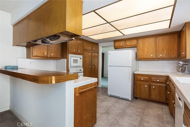 kitchen with light countertops, decorative backsplash, brown cabinetry, white appliances, and a peninsula