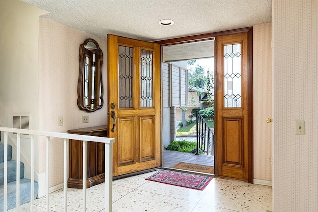 foyer with wallpapered walls, stairs, visible vents, and a textured ceiling