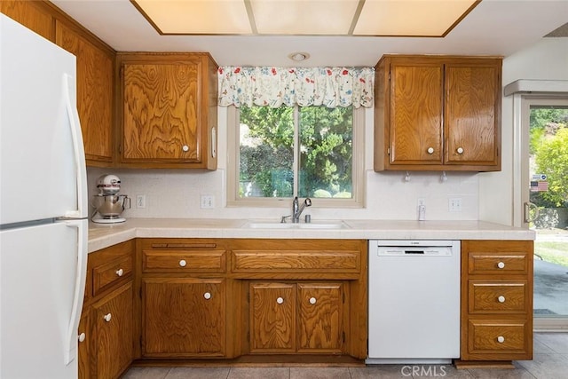 kitchen featuring white appliances, light countertops, a sink, and brown cabinetry