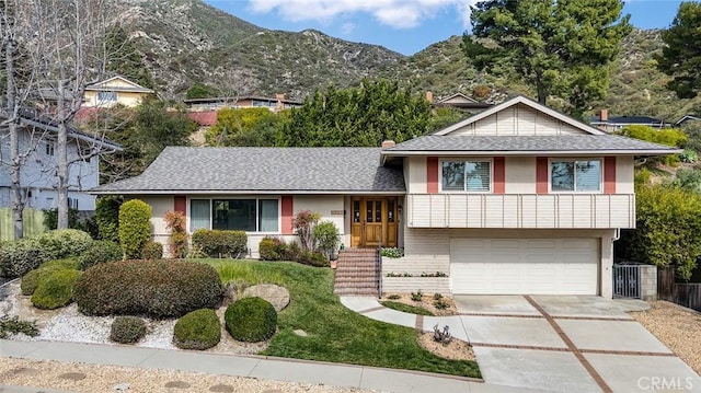 tri-level home featuring roof with shingles, stucco siding, concrete driveway, a mountain view, and a garage