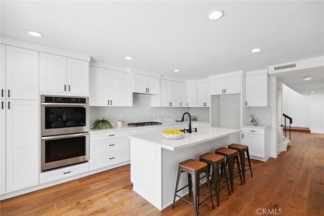 kitchen with stainless steel double oven, a kitchen bar, visible vents, and light wood-style floors