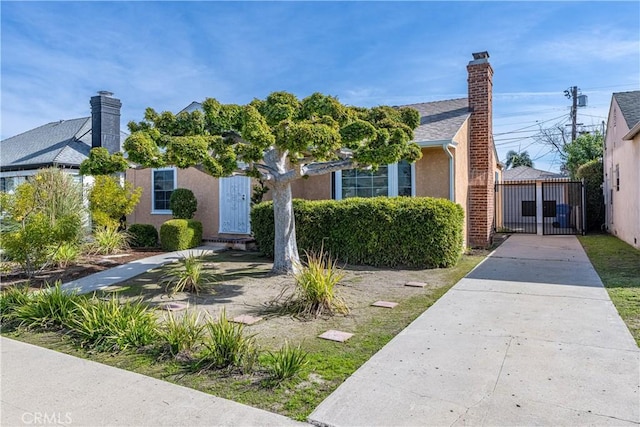 view of front of house with a chimney, fence, a gate, and stucco siding