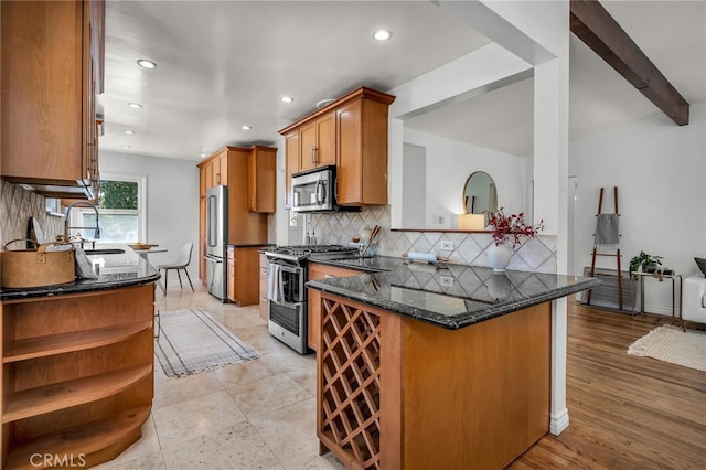 kitchen with appliances with stainless steel finishes, dark stone countertops, a peninsula, open shelves, and a sink